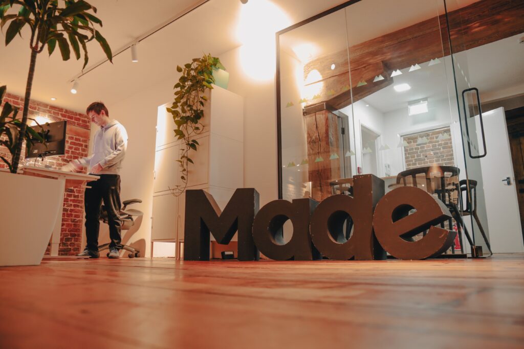 Photo of a person standing and working at a desk next to a large sign that reads Made