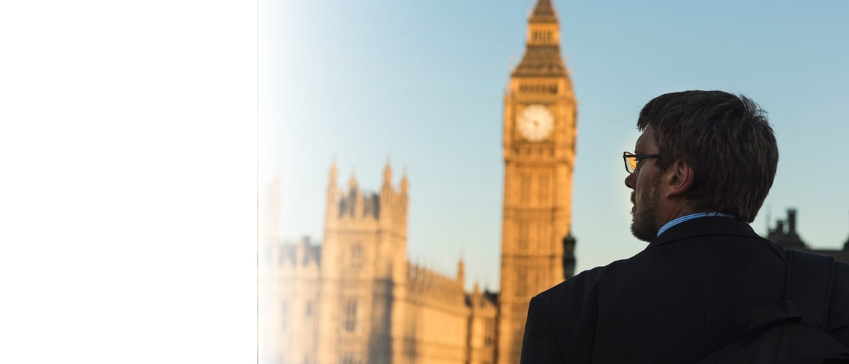 A man in a suit looking at Big Ben and the Houses of Parliament in London during sunset.