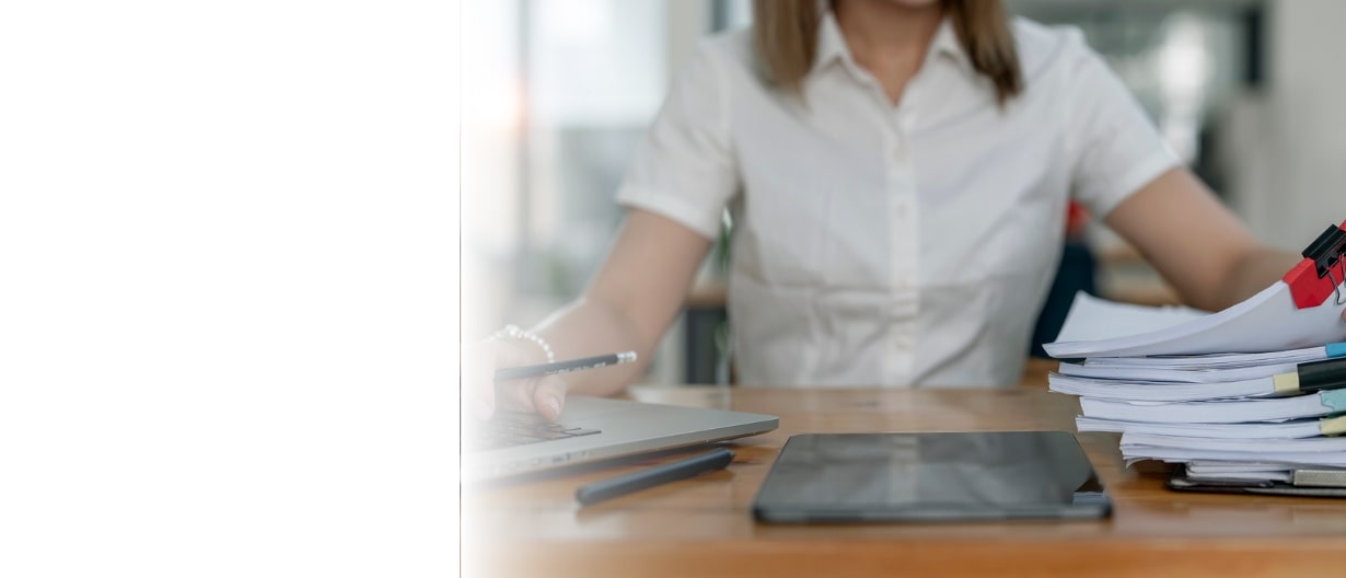 A woman working at a desk with a laptop, organizing a large stack of documents clipped together, in an office environment.