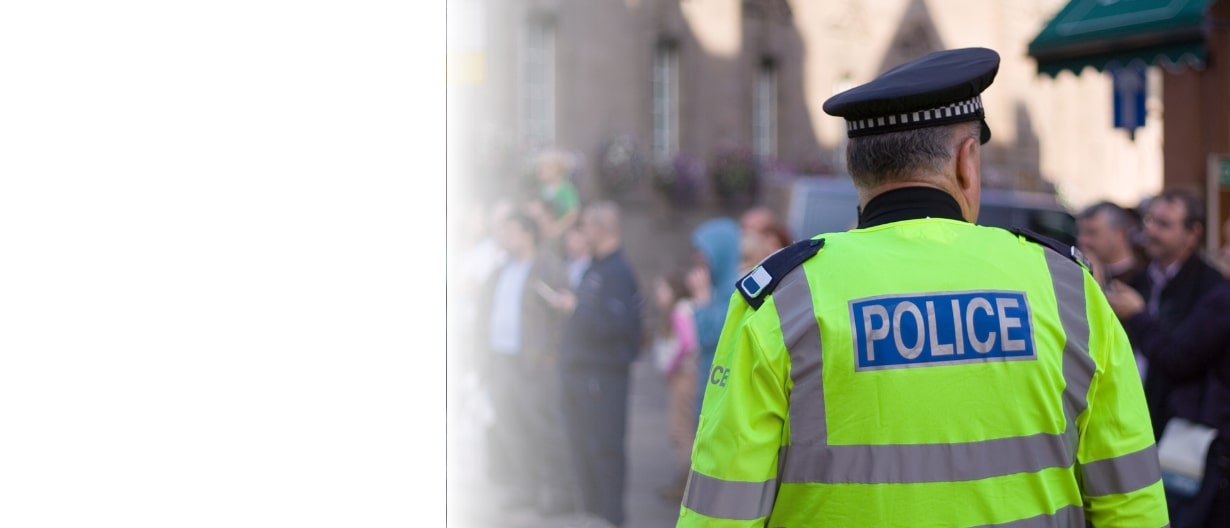 A police officer in a high-visibility jacket monitoring a crowd in a public street during daylight.