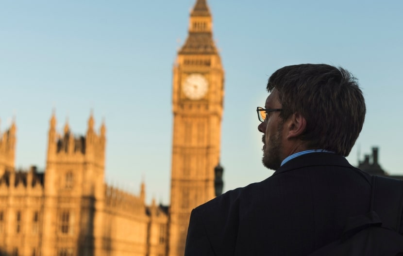 A man in a suit looking at Big Ben and the Houses of Parliament in London during sunset.