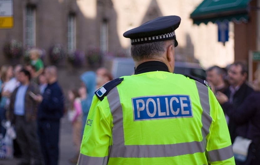 A police officer in a high-visibility jacket monitoring a crowd in a public street during daylight.