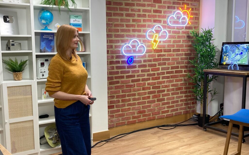 Helena is giving a presentation at the Met Office, she is standing up wearing a mustard-coloured jumper.