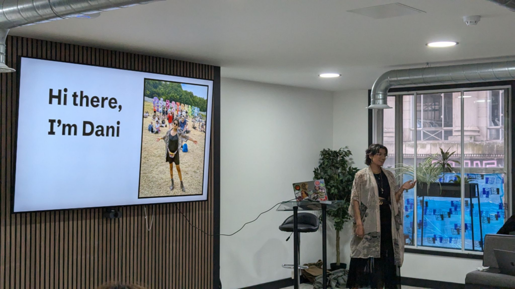 Dani Swift presents in front of a screen that says 'Hi there, I'm Dani'. She is standing and smiling at the audience.